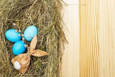 Söğüt yapraklı samanlıkta paskalya yumurtası kavramı ve tahta masa arkasında kağıttan tavşan hediyesi.