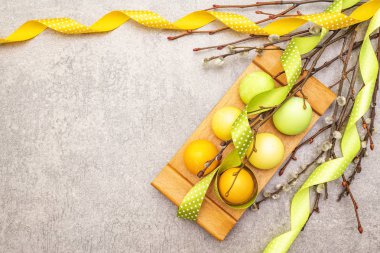 Paskalya yumurtaları, söğüt ağacı dalları, benekli saten kurdeleler. Tahta bir arka planda ahşap bir stantta kavram, üst görünüm, boşluğu kopyala.