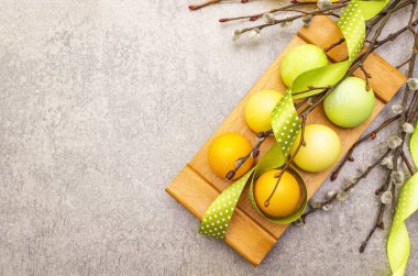 Paskalya yumurtaları, söğüt ağacı dalları, benekli saten kurdeleler. Tahta bir arka planda ahşap bir stantta kavram, üst görünüm, boşluğu kopyala.