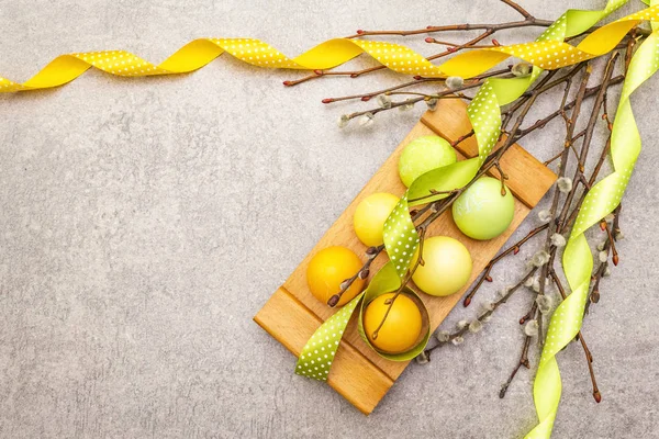 Easter eggs, willow seals branches, polka dot satin ribbons. Concept on a wooden stand on a stone background, top view, copy space. — Stock Photo, Image