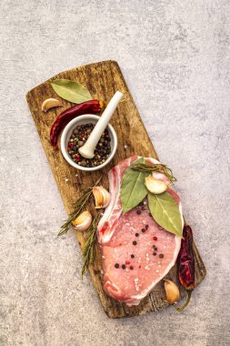 Baharatlı çiğ domuz bifteği ve eski ahşap tahtada kurutulmuş otlar. Tuz, sarımsak, acı biber, biberiye, seramik havan ve bir taş zemin üzerinde tokmak, üst manzara, kapat.