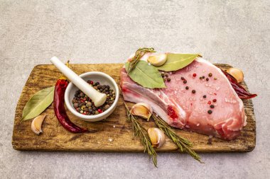 Baharatlı çiğ domuz bifteği ve eski ahşap tahtada kurutulmuş otlar. Tuz, sarımsak, acı biber, biberiye, seramik havan ve kabuklu defne yaprağı..