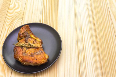 Baharatlı ve otlu domuz bifteği. Ahşap bir arka planda siyah bir plaka içinde.