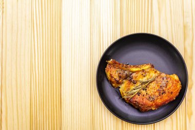 Baharatlı ve otlu domuz bifteği. Ahşap bir arka planda, siyah bir levhada, en üstte.