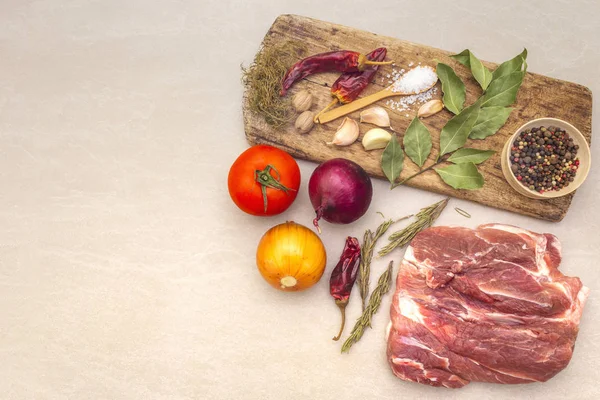 Raw pork shoulder. Spices, dry herbs, onions, garlic, rosemary, bay leaf, nutmeg, pepper mix, tomatoes. Ingredients for marinating meat. Wooden vintage board, stone background, copy space, top view. — Stock Photo, Image