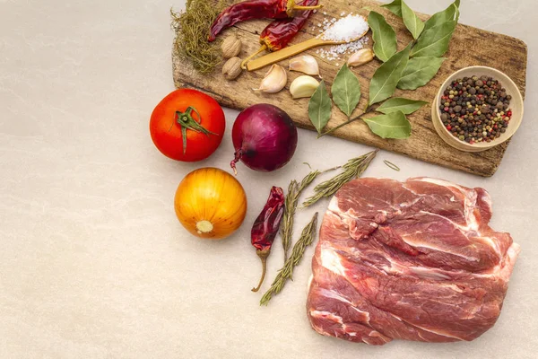 Raw pork shoulder. Spices, dry herbs, onions, garlic, rosemary, bay leaf, nutmeg, pepper mix, tomatoes. Ingredients for marinating meat. Wooden vintage board, stone background, close up, top view. — Stock Photo, Image