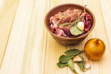 Çiğ domuz omzu. Baharatlar, kuru otlar, sarımsak, biberiye, defne yaprağı, acı biber, hindistan cevizi, biber, soğan, tuz. Salamura et için gerekli malzemeler. Ahşap zemin üzerinde Rustik seramik kase, kopyalama alanı