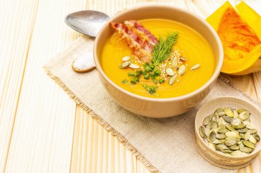 Ev yapımı sıcak sonbahar balkabağı kremalı çorba önlüklü pastırma ve tohumlu. Çiğ balkabağı, taze soğan, dereotu, kaşıkta tuz, ahşap arka planda eski keten kumaş, kapat..