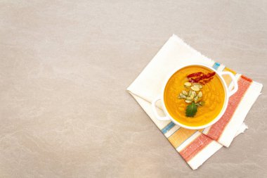 Balkabağı kremalı çorba. Taze kabaklı beyaz seramik kase, kuru tohumlar, tütsülenmiş pastırma. Taş zemin üzerinde kaliteli keten kumaş (peçete) ile, üst görünüm