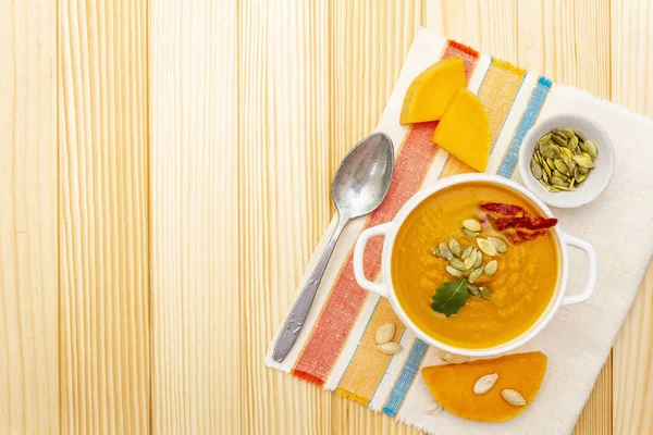 Sopa de creme de abóbora. Tigela de cerâmica branca com abóbora fresca, sementes de abóbora seca, bacon defumado, erva. Com pano de linho vintage (guardanapo) em fundo de madeira, vista superior — Fotografia de Stock