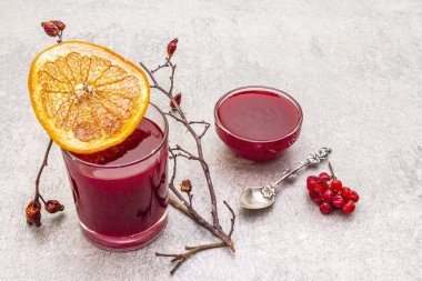 Doğal taze organik içecekler ve viburnum, yaban gülü ve greyfurttan yapılmış reçel. Taş bir arka planda bir bardakta. Köpek gülü dalları, kurutulmuş greyfurt.