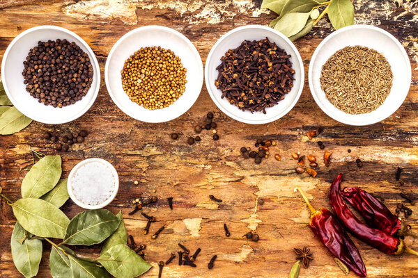Набор различных специй и трав - черный перец, овсянка, розмарин, тмин, острый перец, лавровый лист, кориандр, соль. На деревянном фоне коры, вид сверху
.