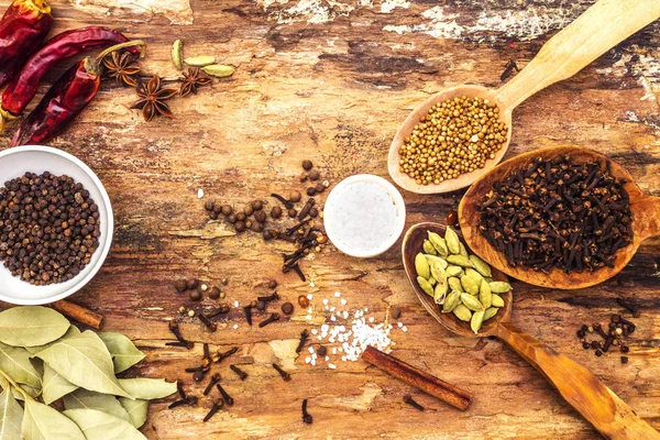 Set of different spices and herbs - black pepper, allspice, hot pepper, bay leaf, coriander, cardamom, star anise, cinnamon sticks, salt. On wooden bark background, top view. — Stock Photo, Image