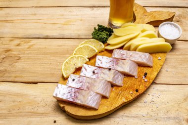 Tahta ve masada balık ve patates kızartması var. Geleneksel İngiliz yemeği, bir bardak bira.