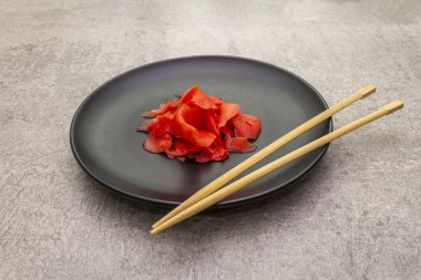 Turşulu suşi, siyah tabakta zencefil dilimleri ve taş zeminde çubuklar.