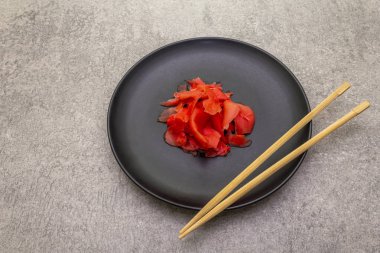 Siyah tabakta turşulu zencefilli suşi dilimleri ve taştan arka planda çubuklar.