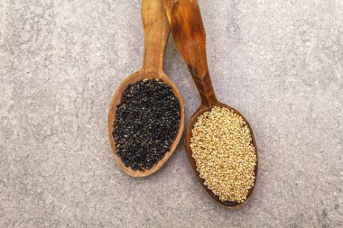 Tahta kaşıklarda beyaz ve siyah susam tohumları taş arka planda, üst manzara, kapat.