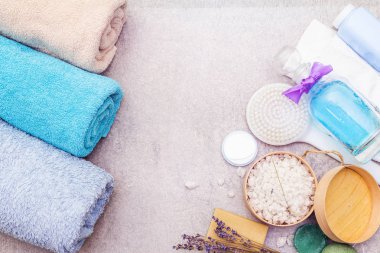Spa seti, doğal malzemeler. Banyo havluları, lavantalı deniz tuzu, doğal zeytin sabunu, duş jeli, krema ve fırça. Taş bir arkaplanda, üst görünüm
