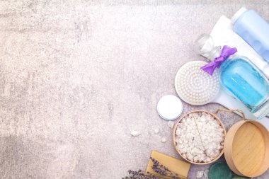 Spa seti, doğal malzemeler. Banyo havluları, lavantalı deniz tuzu, doğal zeytin sabunu, duş jeli, krema ve fırça. Taş bir arkaplanda, üst görünüm
