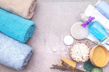 Spa seti, doğal malzemeler. Banyo havluları, lavantalı deniz tuzu, doğal zeytin sabunu, duş jeli, krema ve fırça. Taş bir arkaplanda, üst görünüm