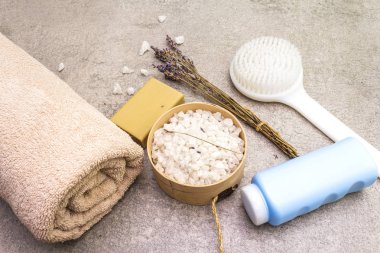 Spa konsepti, doğal malzemeler. Banyo havlusu, lavantalı deniz tuzu, doğal zeytin sabunu, duş jeli ve fırça. Taş bir arkaplanda, üst görünüm