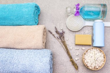 Spa konsepti, doğal malzemeler. Banyo havluları, lavantalı deniz tuzu, doğal zeytin sabunu, duş jeli ve fırça. Taş bir arkaplanda, üst görünüm.