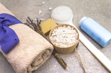 Spa konsepti, doğal malzemeler. Banyo havlusu, lavantalı deniz tuzu, doğal zeytin sabunu, duş jeli ve fırça. Taş bir arkaplanda, üst görünüm