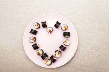 Romantik kalp suşi yemeği. Somon, Philadelphia peyniri ve salatalıklı rulo. Sevgililer Günü ya da 8 Mart için konsept. Pembe tabakta, taş arka planda, en üstte
