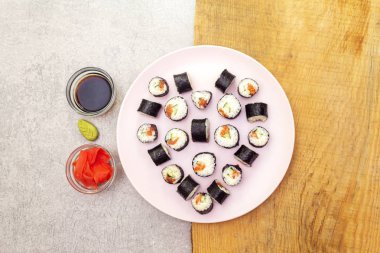 Romantik kalp suşi yemeği. Maki, zencefilli, wasabi ve soya soslu, pembe tabakta. Sevgililer Günü ya da 8 Mart için konsept. Taş ve ahşap zemin, üst manzara