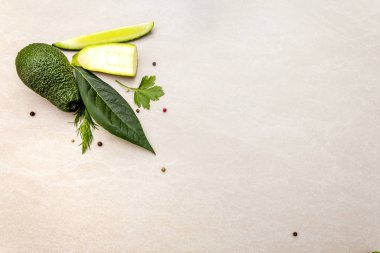 Yeşil sebzeler ve şifalı bitkiler. Avokado, avokado yaprağı, salatalık, kabak, maydanoz, dereotu, yeşil soğan tüyü, biber karışımı. Taş zeminde, düz yerde, en üstte.