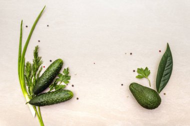 Green vegetables and herbs cooking background. Avocado, avocado leaf, cucumber, parsley, dill, green onion feathers, peppers mix. On a stone background, flat lay, top view
