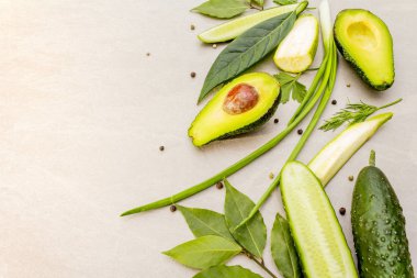 Yeşil sebzeler ve şifalı bitkiler. Avokado, avokado yaprağı, defne yaprağı, salatalık, kabak, maydanoz, dereotu, yeşil soğan tüyü, biber karışımı. Taş bir arka planda, düz yatıyordu.