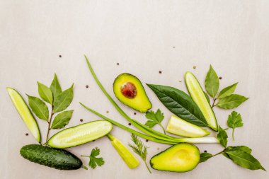 Yeşil sebzeler ve şifalı bitkiler. Avokado, avokado yaprağı, defne yaprağı, salatalık, kabak, maydanoz, dereotu, yeşil soğan tüyü, biber karışımı. Taş zeminde, düz yerde, en üstte..