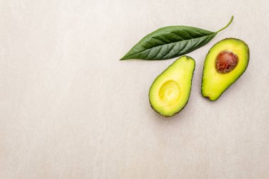 Avokado, ikiye bölünmüş, kemik ve avokado yaprağı ile. Aşçılık geçmişi. Taş yüzeyde, üst manzara