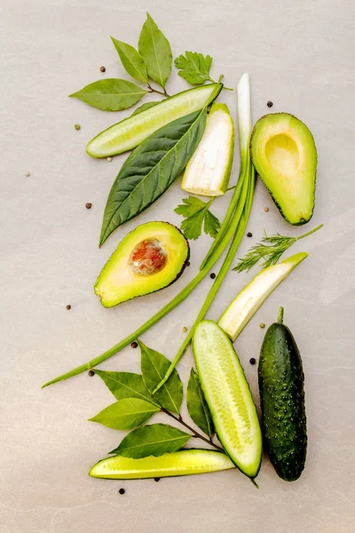 Green vegetables and herbs cooking background. Avocado, avocado leaf, bay leaf, cucumber, zucchini, parsley, dill, green onion feathers, peppers mix. On a stone background, flat lay, top view. — Stock Photo, Image