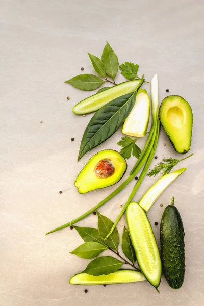 Green vegetables and herbs cooking background. Avocado, avocado leaf, bay leaf, cucumber, zucchini, parsley, dill, green onion feathers, peppers mix. On a stone background, flat lay, top view. — Stock Photo, Image