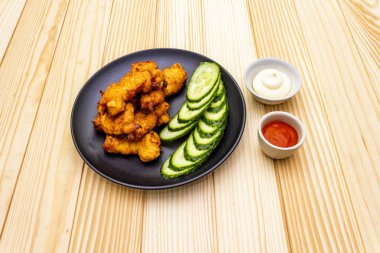 Chicken fried (nuggets) homemade on black plate with two sauces - mayonnaise and hot spicy sauce. On wooden background