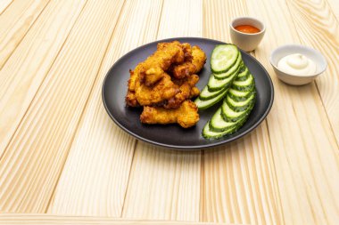 Chicken fried (nuggets) homemade on black plate with two sauces - mayonnaise and hot spicy sauce. On wooden background