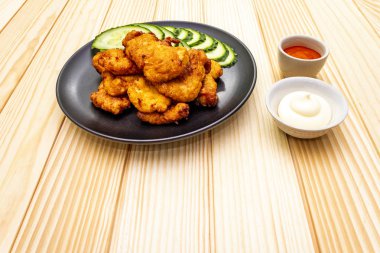Chicken fried (nuggets) homemade on black plate with two sauces - mayonnaise and hot spicy sauce. On wooden background
