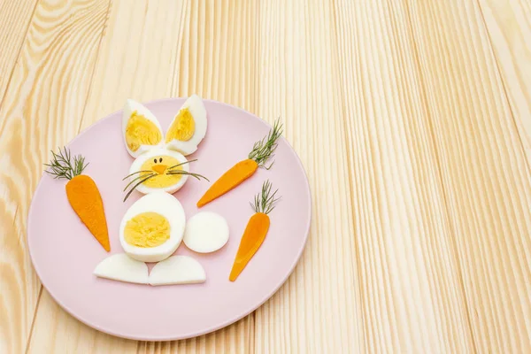 Zajączek wielkanocny (królik) i jaj kurzych dzieci (dzieci) koncepcja żywności. Z marchewką na różowym talerzu. Drewniane tło, widok z góry — Zdjęcie stockowe