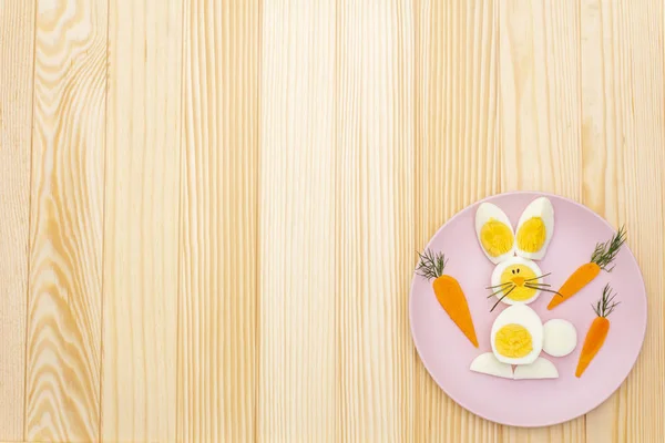 Easter bunny (rabbit) and chicken eggs children (kids) food concept. With carrot on rosy (pink) plate. Wooden background, top view
