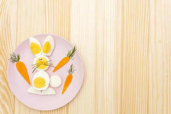 Easter bunny (rabbit) and chicken eggs children (kids) food concept. With carrot on rosy (pink) plate. Wooden background, top view