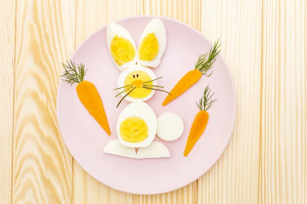 Easter bunny (rabbit) and chicken eggs children (kids) food concept. With carrot on rosy (pink) plate. Wooden background, top view