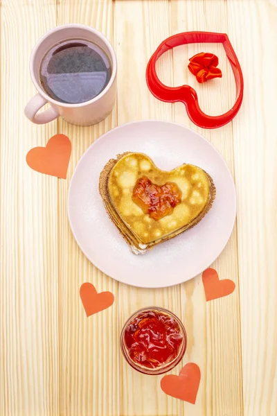 Оладьи в форме сердца для романтического завтрака с клубничным джемом и черным чаем. Масленица (карнавал) концепция. На деревянном фоне, вид сверху — стоковое фото