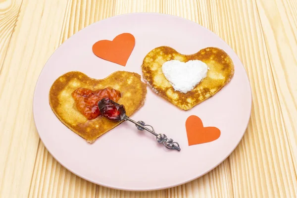 Heart shaped pancakes for romantic breakfast with strawberry jam, silver spoon and paper hearts. Shrovetide (carnival) concept. On wooden background — Stock Photo, Image