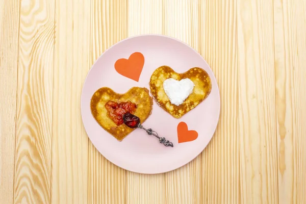 Crêpes en forme de coeur pour le petit déjeuner romantique avec confiture de fraises, cuillère en argent et coeurs en papier. Concept de Shrovetide (carnaval). Sur fond bois, vue de dessus — Photo