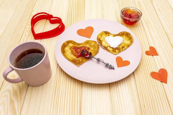 Heart shaped pancakes for romantic breakfast with strawberry jam and black tea. Shrovetide (carnival) concept. On wooden background — Stock Photo, Image