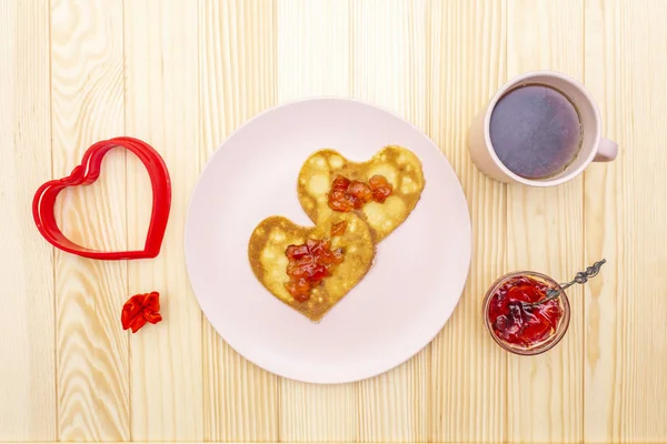 Crêpes en forme de coeur pour un petit déjeuner romantique avec confiture de fraises et thé noir. Concept de Shrovetide (carnaval). Sur fond bois, vue de dessus — Photo
