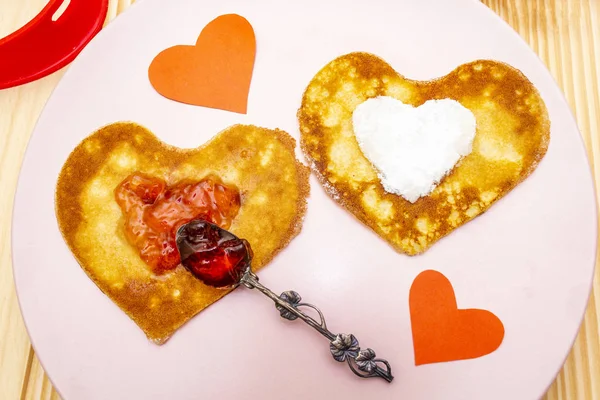 Crêpes en forme de coeur pour le petit déjeuner romantique avec confiture de fraises, cuillère en argent et coeurs en papier. Concept de Shrovetide (carnaval). Sur fond bois, vue de dessus — Photo