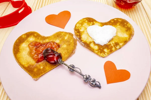 Оладьи в форме сердца для романтического завтрака с клубничным вареньем, серебряной ложкой и бумажными сердцами. Масленица (карнавал) концепция. На деревянном фоне — стоковое фото